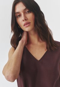 Bordo bezrukavni top s V-izrezom, izrađen od teksturiranog materijala. Karakterizira ga minimalno šivanje i opušteni kroj.