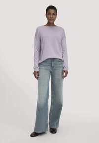 Übergroßer lila Pullover mit langen Ärmeln und weitem Ausschnitt, kombiniert mit hellblauen, weit geschnittenen Jeans und braunen Stiefeletten.