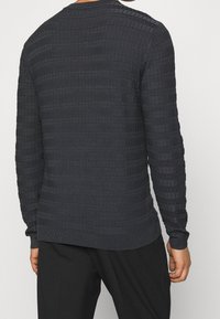 Ciemnoszary, teksturowany sweter dzianinowy z prążkowanymi akcentami i okrągłym dekoltem. Posiada prostokątny wzór na całej tkaninie.