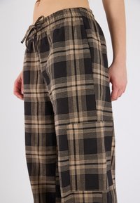 Zwarte en beige geblokte broek met een relaxed fit, elastische tailleband en trekkoord. Beschikt over zijzakken en een zacht, textuurgegeven katoenen materiaal.