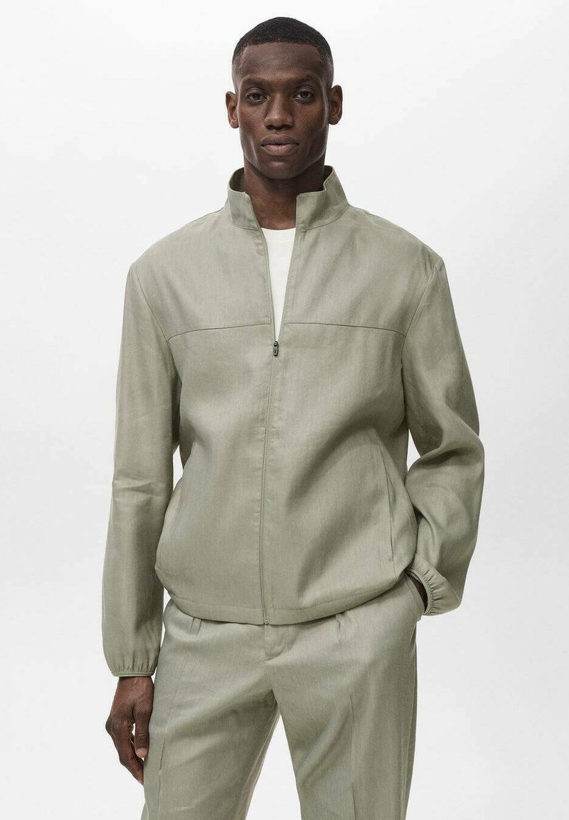 Ljusgrön, zip-up jacka med hög krage, slät textur och två horisontella sömmar över bröstet. Långa ärmar med elastiska manschetter.