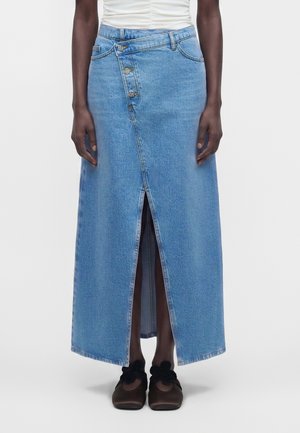 Denim midi nederdel med asymmetrisk knaplukning og frontslids, båret med sorte sko med blomsterdetaljer og hvid rynket top.