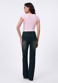 Haut rose côtelé ajusté associé à un jean évasé bleu foncé avec taille mi-haute et poches arrière classiques.