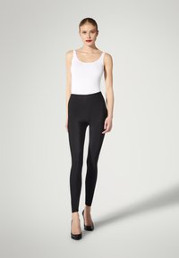 Sorte leggins lavet af strækbart materiale, med en høj talje og en glat tekstur, parret med en hvid tanktop og sorte hæle.