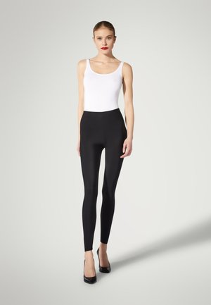 Svarta leggings i stretchmaterial, med hög midja och slät yta, kombinerat med en vit linne och svarta klackar.
