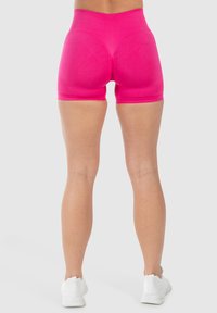 Fitted roze sportshorts met een brede tailleband, een soepele textuur en een lengte tot halverwege de dij, gecombineerd met witte sportschoenen.