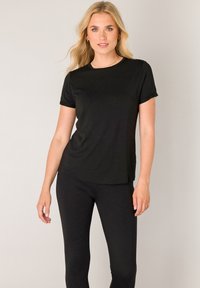 Schwarzes T-Shirt mit kurzen Ärmeln aus einem weichen, leichten Stoff. Leicht lockere Passform mit Rundhalsausschnitt. Kombiniert mit passenden schwarzen Leggings.