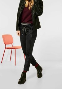 Svarta joggerbyxor med dragsko i midjan, fickor med dragkedja och ribbade röda detaljer vid anklarna, bärs tillsammans med en vinröd tröja och en svart läderjacka.