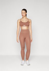 Braun gerippter Sport-BH und hochgeschnittene Leggings aus elastischem Material. Einfaches Design mit dünnen Trägern und minimaler Beschriftung.