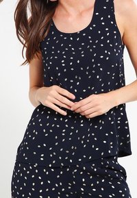 Haut sans manches marine en tissu léger, présentant des motifs de feuilles métalliques dispersés et une coupe décontractée avec un ourlet incurvé.