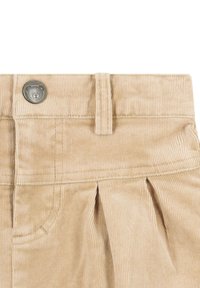 Pantalones cortos de pana beige que presentan un botón metálico con un diseño de oso, pliegues en la cintura y una superficie suave y texturizada.