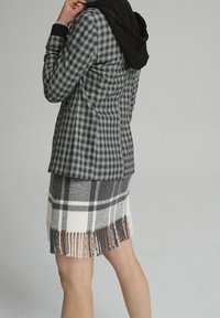 Blazer à carreaux gris et noir associé à une jupe à franges en plaid gris et blanc. L'ensemble présente des textures douces et des motifs distincts.