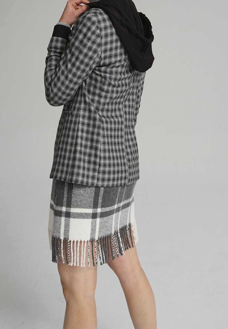Blazer à carreaux gris et noir associé à une jupe à franges en plaid gris et blanc. L'ensemble présente des textures douces et des motifs distincts.