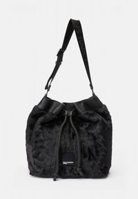 Fekete műszőrme vödörtáska összehúzott felsőrésszel, sima bőr díszítésekkel, állítható pánttal és egy márkás címkével az oldalon.