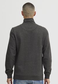 Felpa grigia scura con colletto alto, realizzata in tessuto morbido. Presenta polsini e orlo ribattuti, con una texture liscia e un design minimalista.