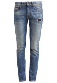 Jean slim bleu délavé avec des patchs usés sur la cuisse droite et le genou gauche, bouton devant, fermeture éclair et style cinq poches.