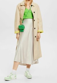 Beżowy trencz, jasn зелony prążkowany crop top, satynowa biała spódnica midi oraz zielone sneakersy z białymi akcentami. Mała zielona torebka na ramię.