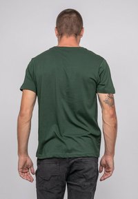 T-shirt en coton vert à manches courtes, col rond et texture lisse, vu de dos, associé à un jean foncé.