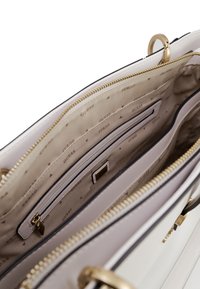 Interno della borsa sintetica bianca con rivestimento in tessuto beige, molteplici scomparti, zip dorata e dettagli brandizzati.