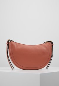 Lille halvmåneformet brun lædertaske med sorte stropdetaljer og guldlynlås, udstillet på en hvid sokkel mod en grå baggrund.