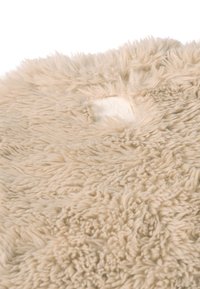 Alfombra cuadrada de piel sintética beige con una textura suave y esponjosa. Presenta una etiqueta sutil en una esquina. Apariencia mullida y voluminosa.