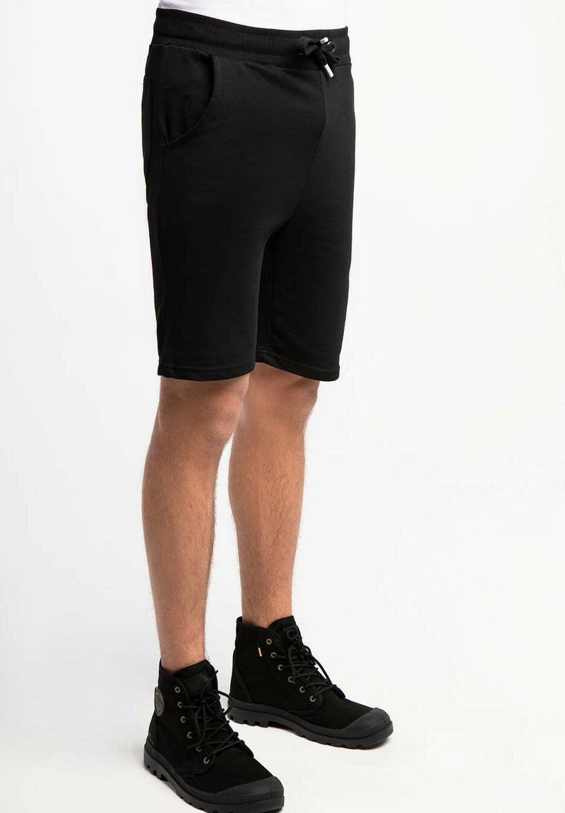 Shorts en tissu noir avec une taille élastique et un cordon de serrage réglable. Comprend deux poches latérales et un design ajusté. Associé à des bottes noires.