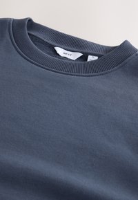 Sötétkék pulóver puha pamutszövetből, bordázott kerek nyakkivágással és finom textúrával, belső nyakrészen címkével.