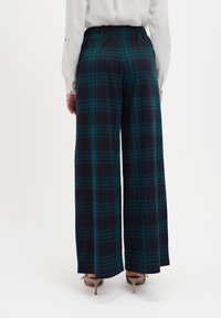 Karierte weite Hose in Dunkelblau und Grün aus leichtem Stoff. Elastischer Bund und eine lockere Passform. Hohe Schuhe sichtbar.