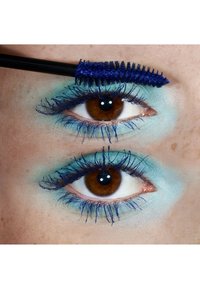 Blaue Mascara auf langen, gewellten Wimpern vor einem hellblauen Lidschatten-Hintergrund. Braune Augen mit sichtbarer Textur und Glanz.