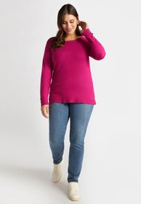 Magenta sweter z okrągłym dekoltem i długimi rękawami, w połączeniu z niebieskimi dżinsami i białymi sneakersami. Gładka tekstura, bez widocznych wzorów.