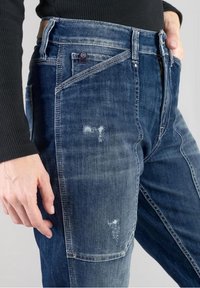 Jeans de mezclilla en azul oscuro con una textura desgastada, que cuentan con un bolsillo delantero y ligeras marcas de uso. Diseñados con un corte recto.