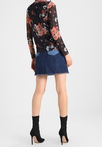 Schwarzes, blumiges Langarm-Oberteil aus transparentem Material, kombiniert mit einem Jeans-Minirock mit ausgefranstem Saum und zwei Gesäßtaschen. Schwarze Ankle Boots.