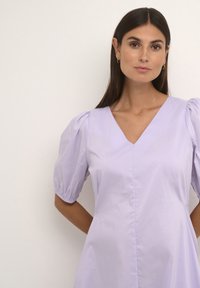 Šviesiai violetinė suknelė su V formos iškirpte, trumpomis pūstomis rankovėmis ir tiesiu kirpimu. Pagaminta iš lengvos medžiagos su lygiu paviršiumi ir minimaliais siūlais.