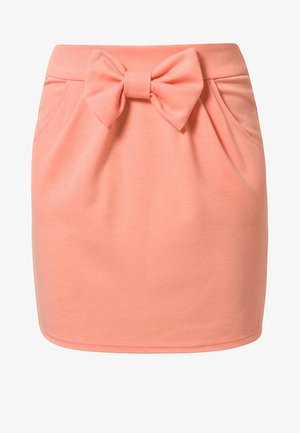 Mini falda rosa suave con bolsillos delanteros y un gran lazo de tela atado a la cintura, textura suave y diseño sencillo.