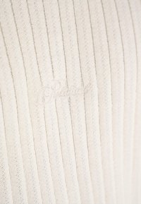 Knitted cream sweater with vertical ribbed texture. Features subtle, embroidered "Pinkwool" logo at the bottom. Soft, lightweight fabric.