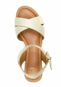 Sandale en cuir beige avec des brides croisées et une boucle à la cheville. Semelle intérieure lisse de couleur noisette et accents texturés subtils sur les brides.