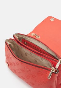 Rød tekstureret håndtaske med to lynlåslommer, guldklemmenheder og et mønstret indre. Lukkemekanismen har en trykknap og kædedetalje.