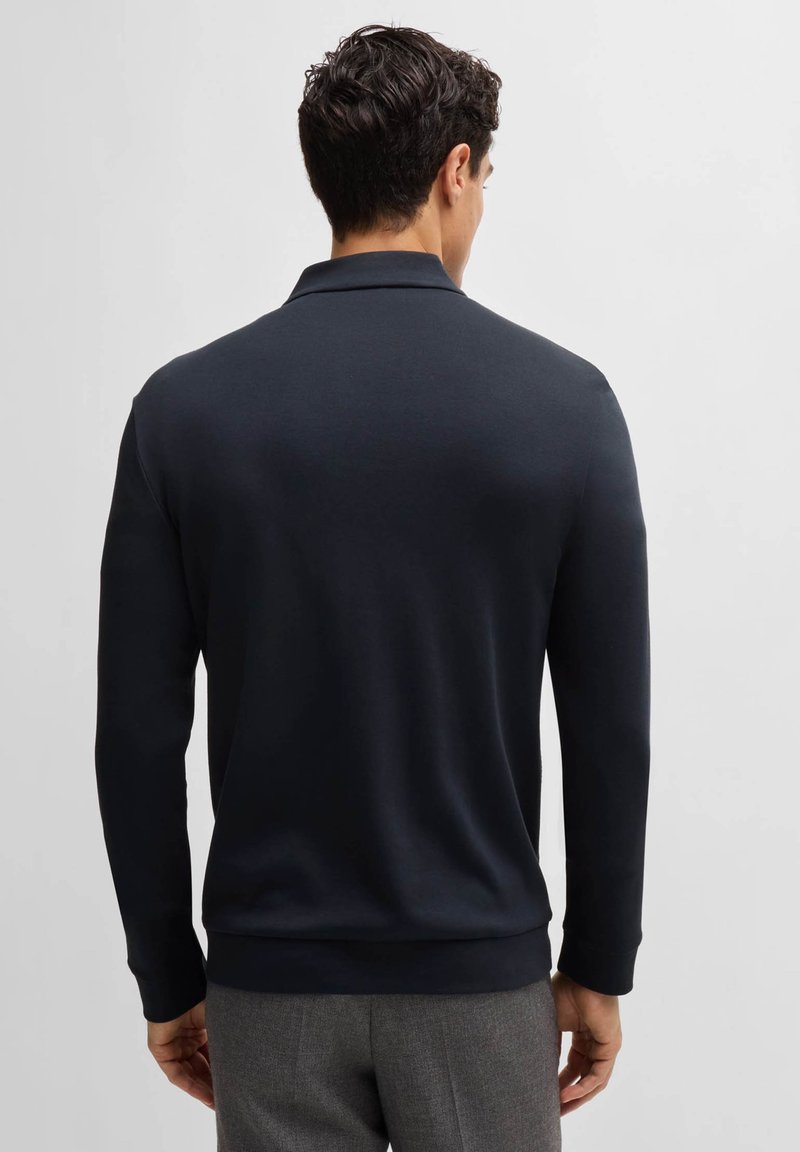 Sweatshirt bleu marine avec col polo, manches longues et poignets côtelés. Texture lisse et design simple sans logos ni motifs visibles.