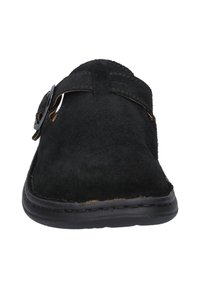 Scarpa nera in suede, tipo slip-on, con punta tonda, presenta un dettaglio con fibbia laterale e suola in gomma nera. Texture morbida e design informale.