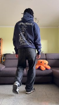 Tumesinine kapuutsiga, millel on lillemuster ja seljal on tekst "Pegador", kombineeritud mustade teksade ja must-valgete spordijalanõudega. Kapi kõrval on mänguasi.