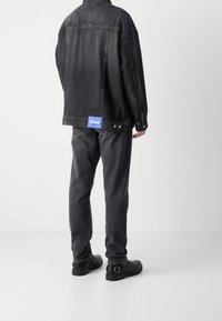 Chaqueta y pantalones de mezclilla negros, con una etiqueta azul "HUGO" en la parte trasera. El conjunto tiene un ajuste relajado y una textura suave. Zapatos negros completan el look.