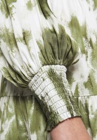 Groen en witte tie-dye stof met geraffineerde pofmouwen en smockdetails aan de manchetten. Zachte textuur, vloeiende vorm, met een soepel silhouet.