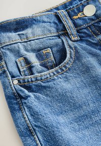 Blaue Jeans aus Denim mit verblasster Textur, Kontrastnähten und einer vorderen Tasche. Merkmale sind ein Metallknopf an der Taille.