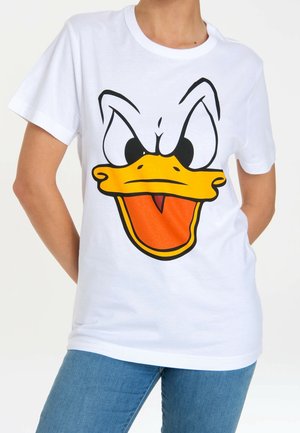 Persona con camiseta blanca con una gran cara de pato de dibujos animados que muestra ojos enfadados y pico naranja abierto, combinada con vaqueros azules.