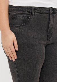 Jeans de mezclilla negra con un diseño ajustado, que cuentan con un bolsillo delantero, presillas para cinturón y una textura suave.