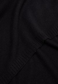 Maglione nero a maglia, texture morbida, polsini e orlo a costine, con una finitura liscia. Il tessuto si drappeggia dolcemente, mettendo in risalto un design semplice e classico.