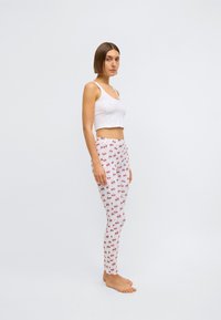 Haut court blanc associé à des leggings moulants ornés d'un motif de cerises sur fond rose clair. Jambes visibles, pieds nus.