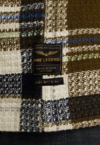 Geweven stof met een ruitpatroon in bruin, blauw en crème, met een gestructureerd oppervlak. Label: PME Legend, "Getest op Grote Hoogte."