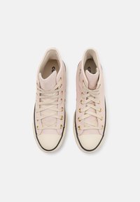 Höga sneakers i blek rosa mocka med beige snören och guldögon. Vit gummitå och svart sula, minimal varumärkesprofil är synlig.