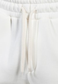 Weiße Baumwoll-Sweatpants mit strukturierter Oberfläche, ausgestattet mit einem elastischen Bund und einer Kordel mit Fischgrätmuster.